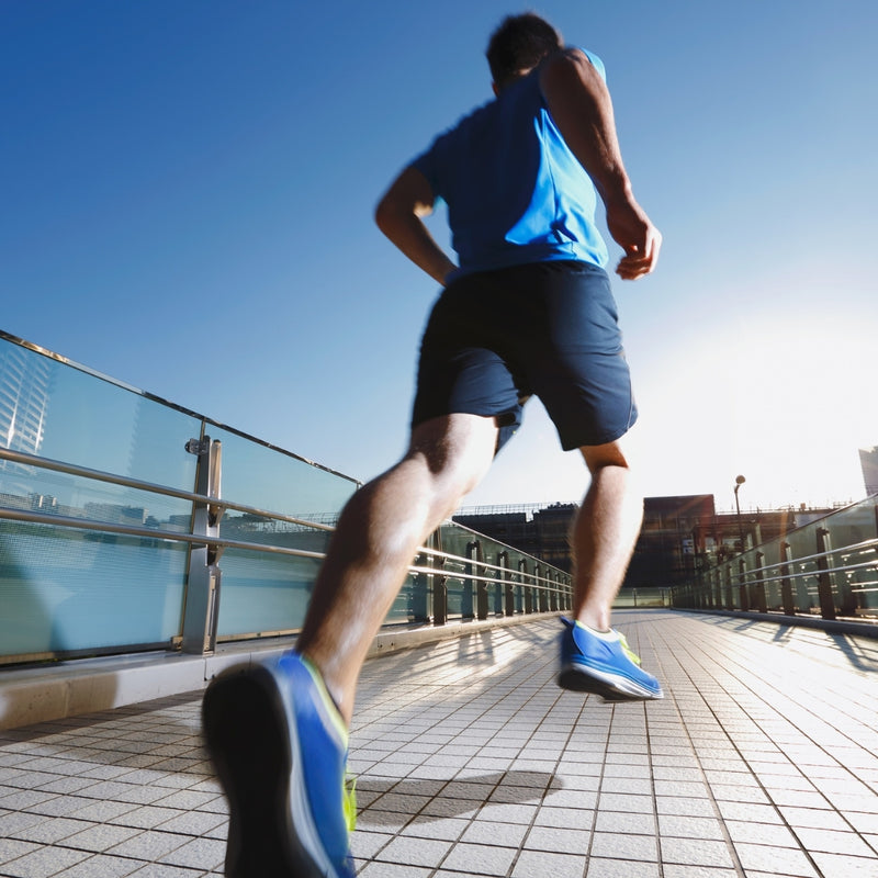 Person running on a sidewalk with a clear blue sky and buildings in the background