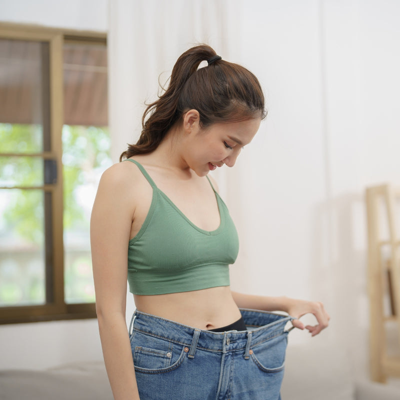 Woman wearing a green sports bra and large blue jeans indoors.